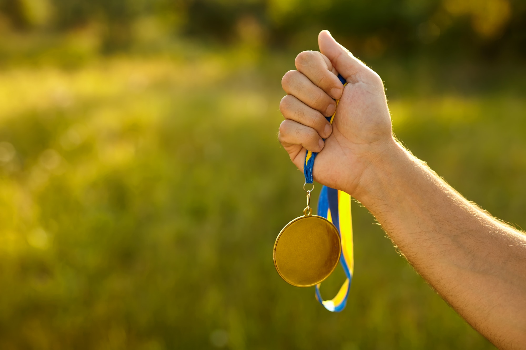 Winner hand holding gold medal with ribbon