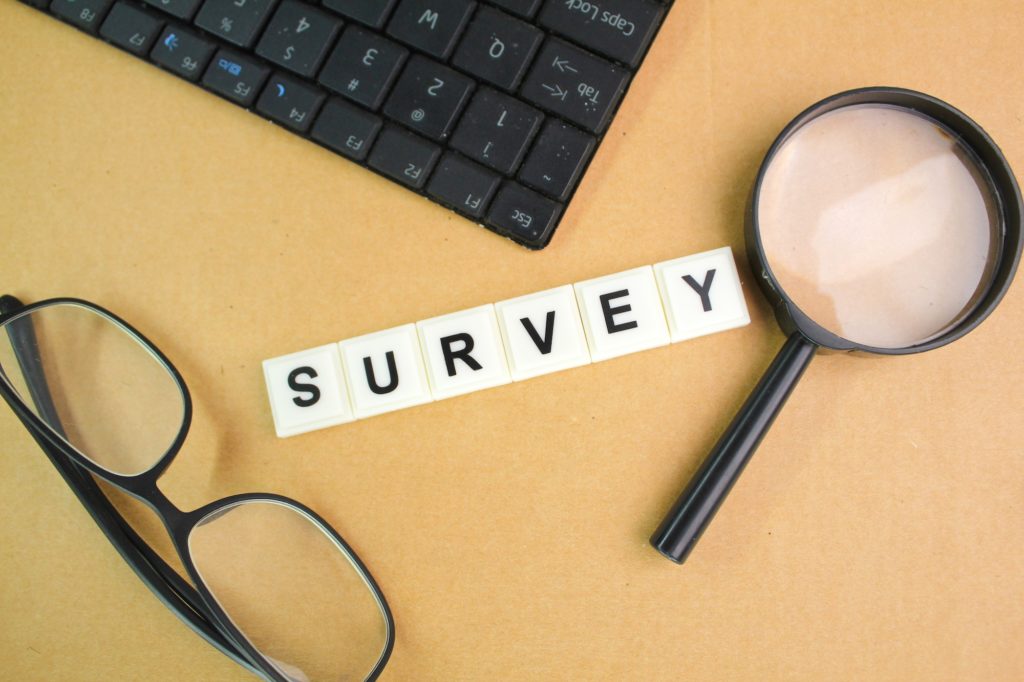 glasses, laptop keyboard and magnifying glass with the word survey.